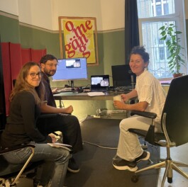 People in a studio editing together a film in a computer on a desk, looking at the person taking the fotograph